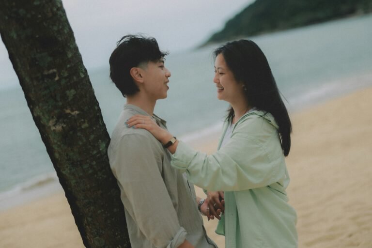 Couple talking on a sandy beach near a tree.